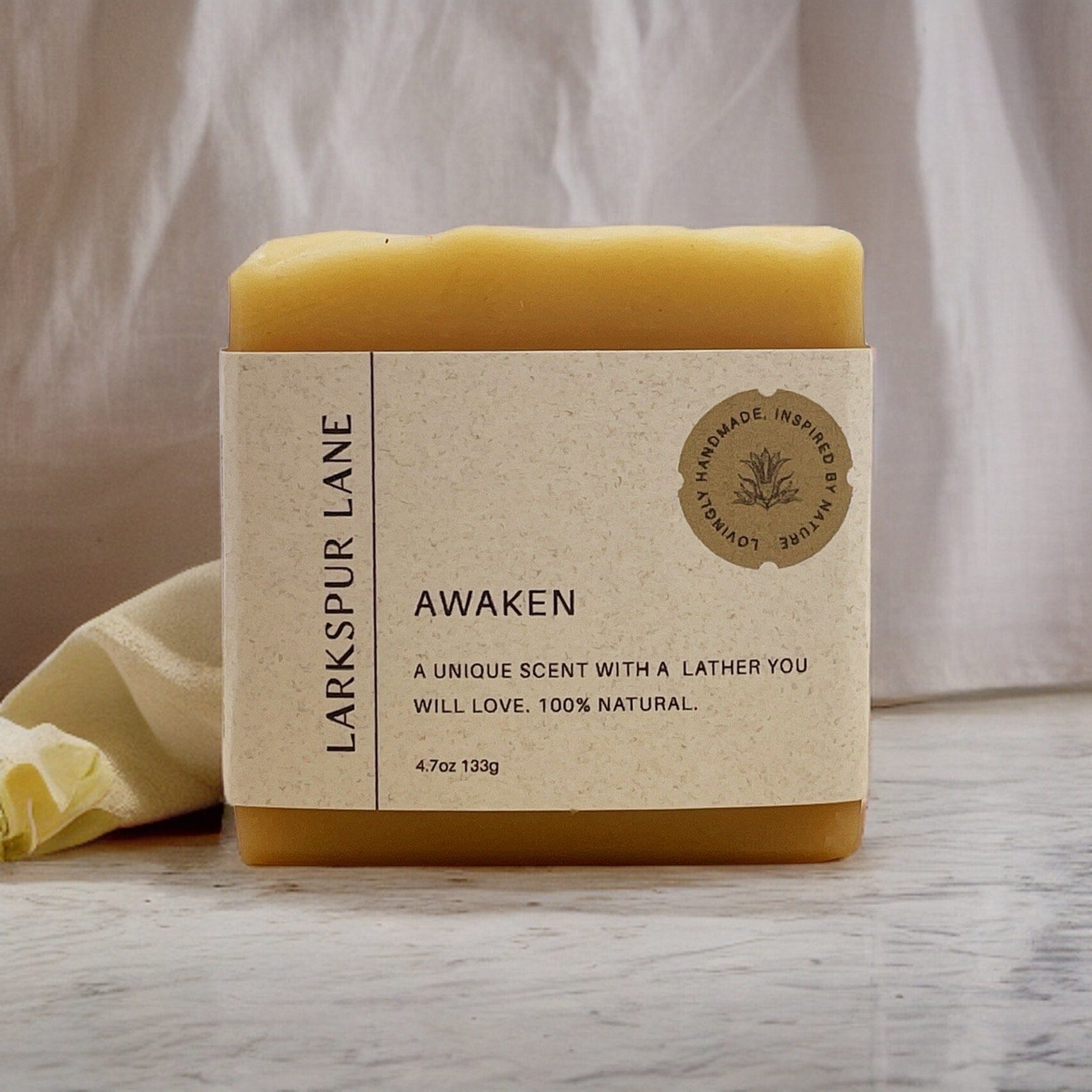 Larkspur Lane’s Awaken soap sitting on a table with a cloth hanging behind it