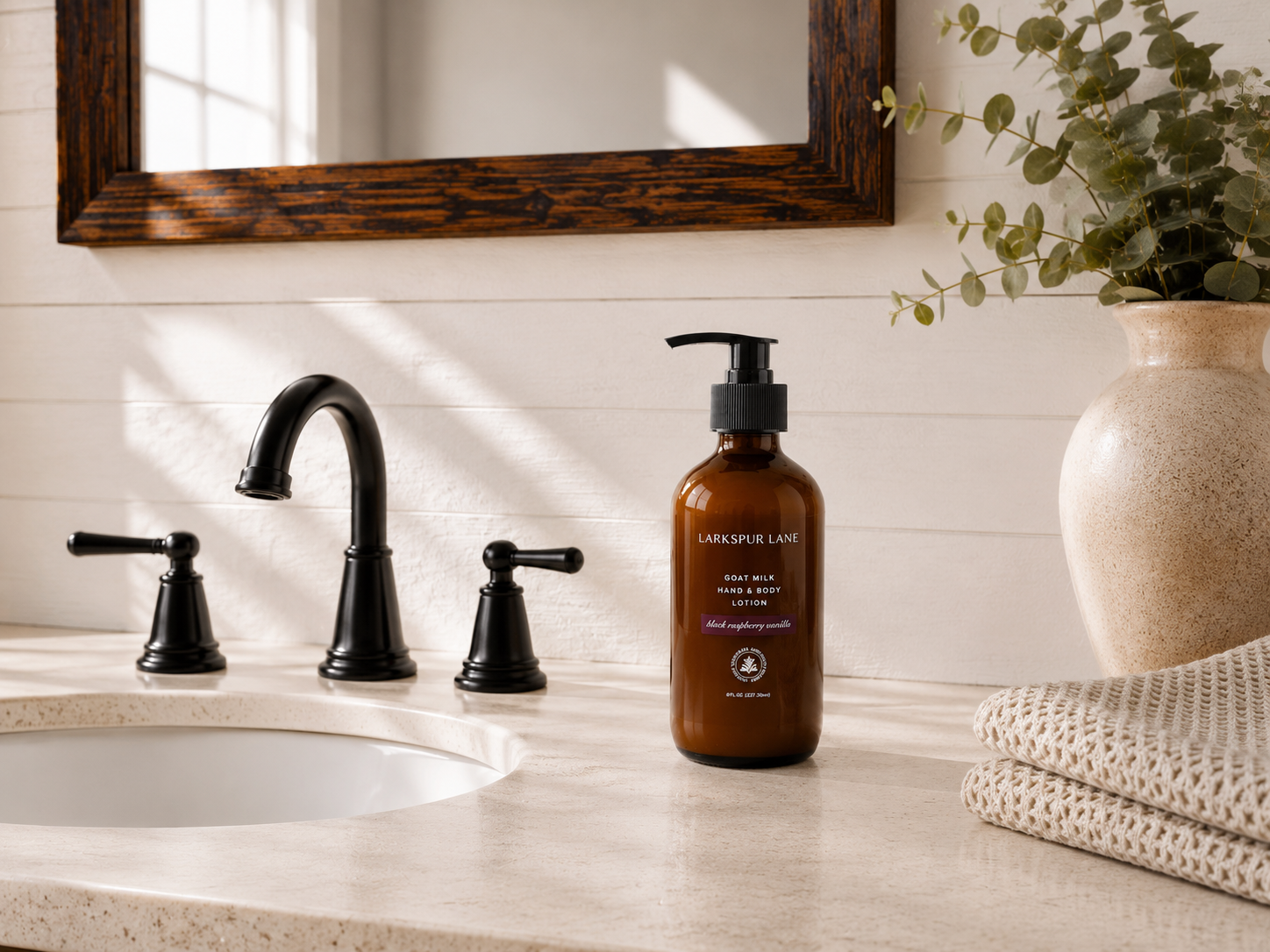 Black Raspberry Vanilla Goat Milk Hand & Body Lotion by Larkspur Lane in an amber glass pump bottle on a bright modern farmhouse bathroom vanity.