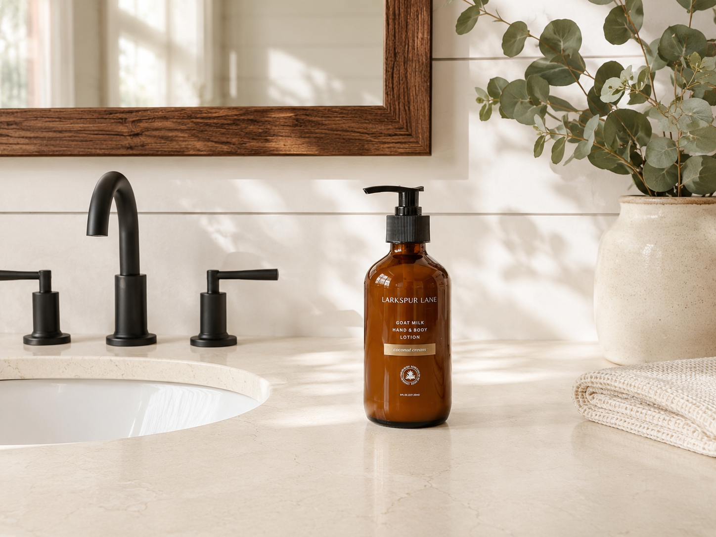 Coconut Cream Goat Milk Hand & Body Lotion by Larkspur Lane in an amber glass pump bottle on a bright modern farmhouse bathroom vanity.