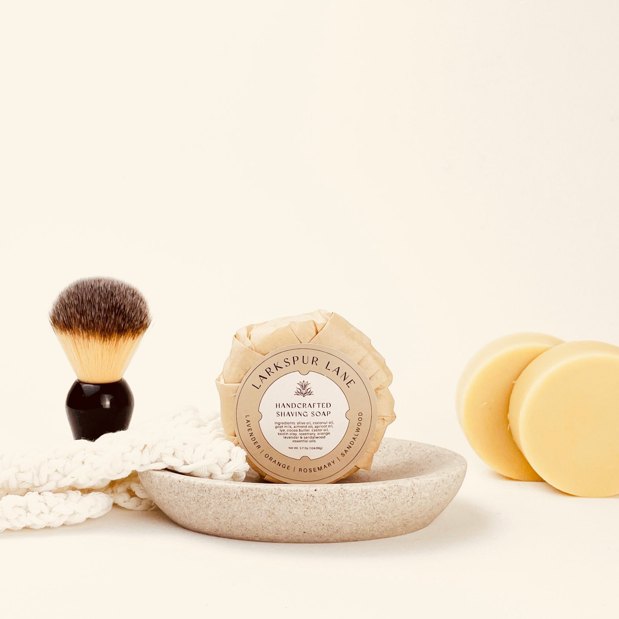 handmade goat milk shave soap puck sitting on a ceramic dish a wet shave brush sitting next to soap