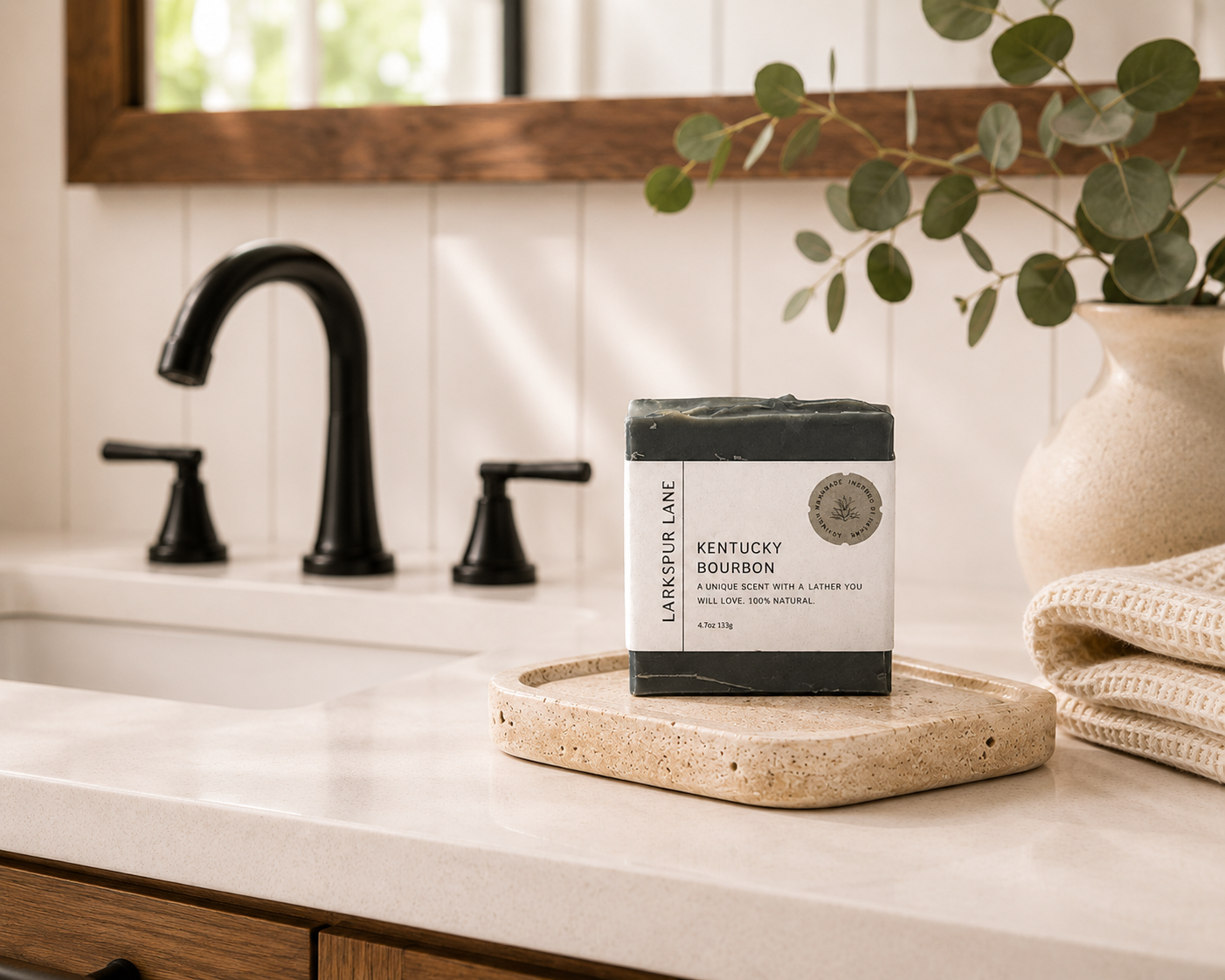 Larkspur Lane Kentucky Bourbon handcrafted soap displayed on a stone soap dish in a bright modern farmhouse bathroom.