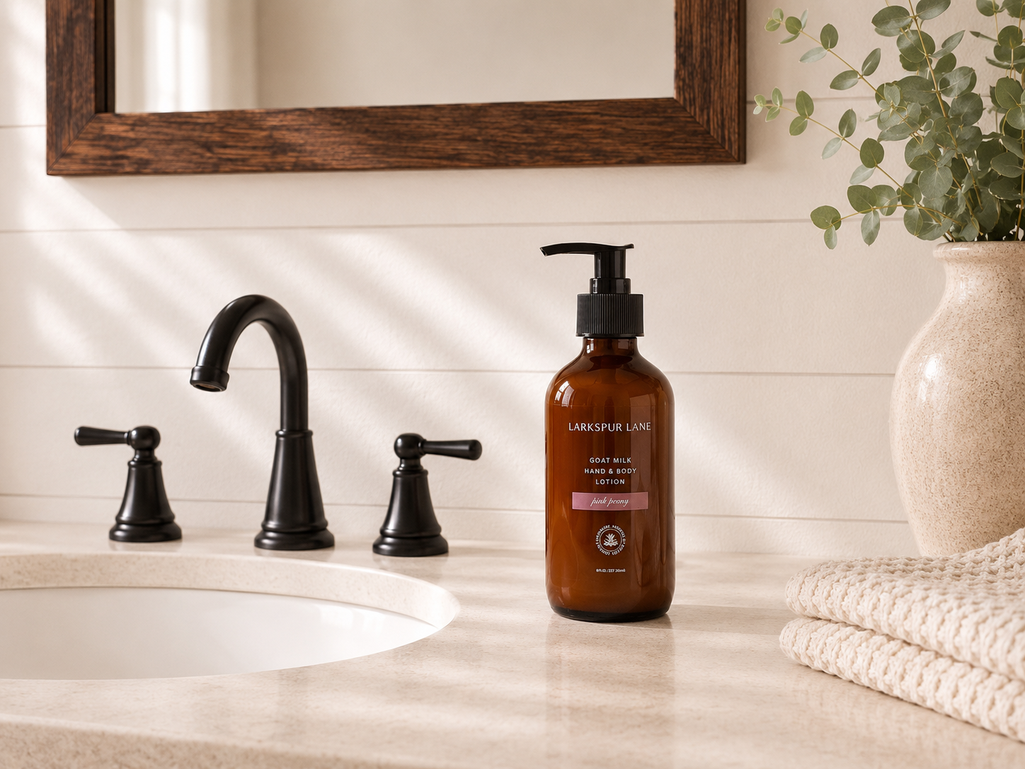 Pink Peony Goat Milk Hand & Body Lotion by Larkspur Lane in an amber glass pump bottle on a bright modern farmhouse bathroom vanity.